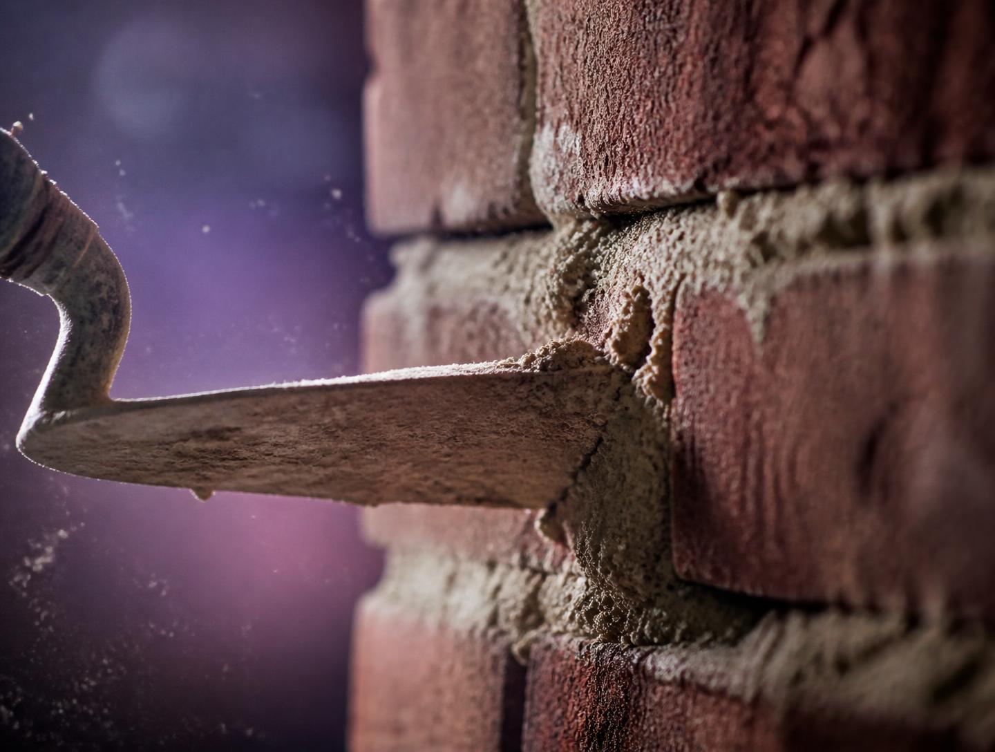 Trowel pressing fresh mortar into brickwork joints